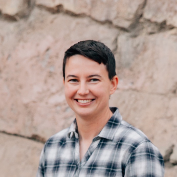 Elayne Petterson smiling in front of a stone wall.
